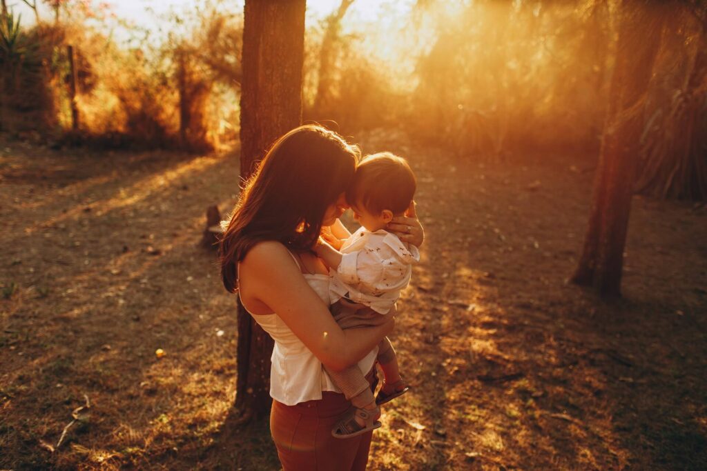 子どもを抱きしめる母親のイメージ写真。夕暮れの自然の中で親子が向き合っている。